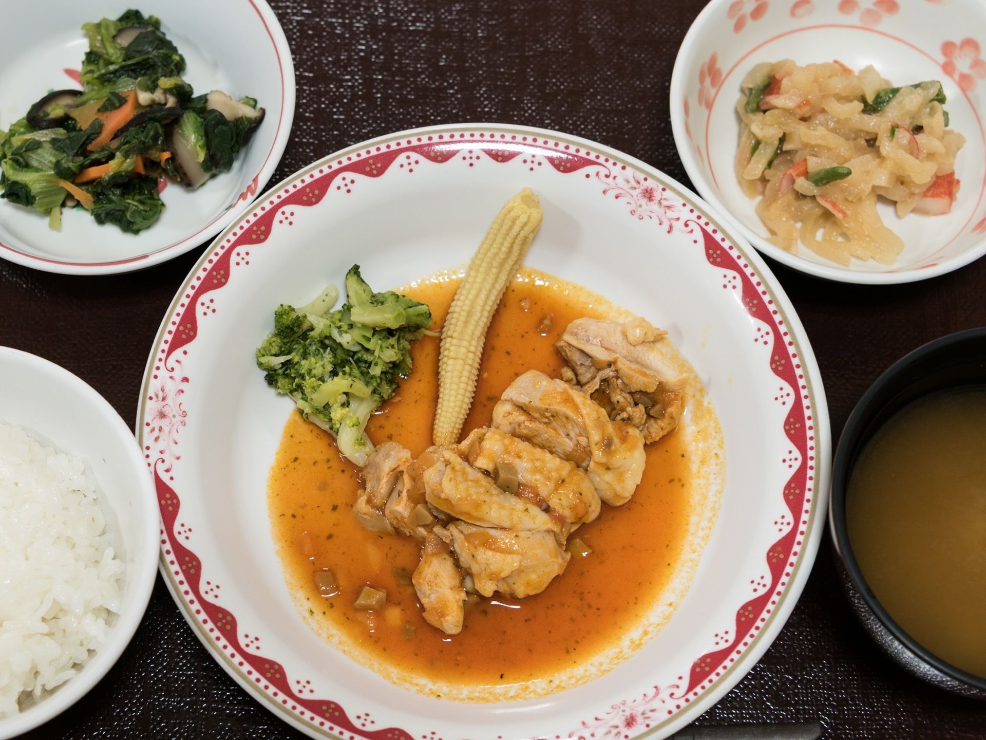 黒いお盆の上には5品の食事が用意されている。メインは鶏肉で、同じお皿にはゆでられたヤングコーンやブロッコリーが添えられている。