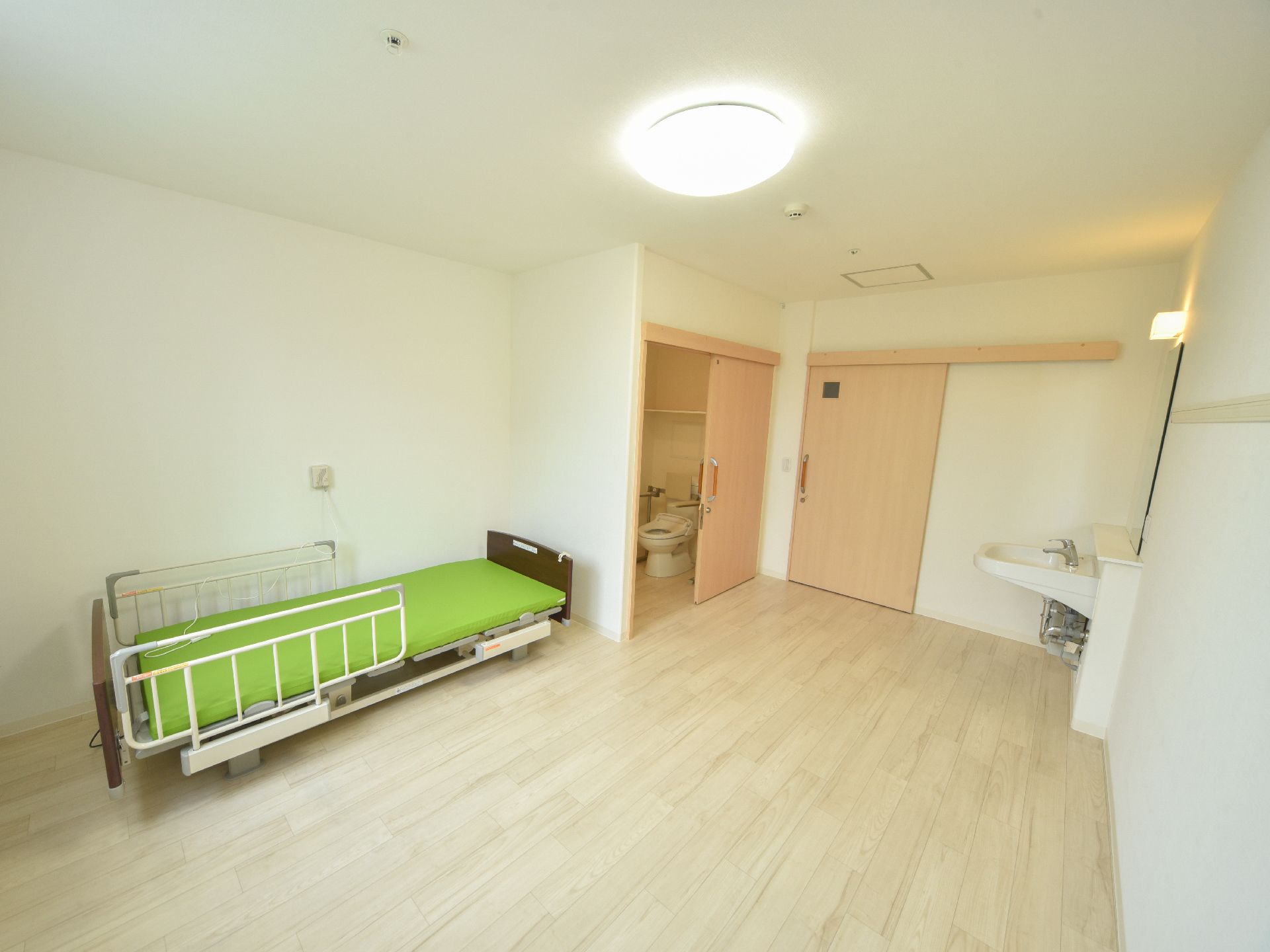 左側にはベッドがある。その近くには扉があり、そこの中はトイレになっている。右側には洗面台がある。床はフローリングになっている。