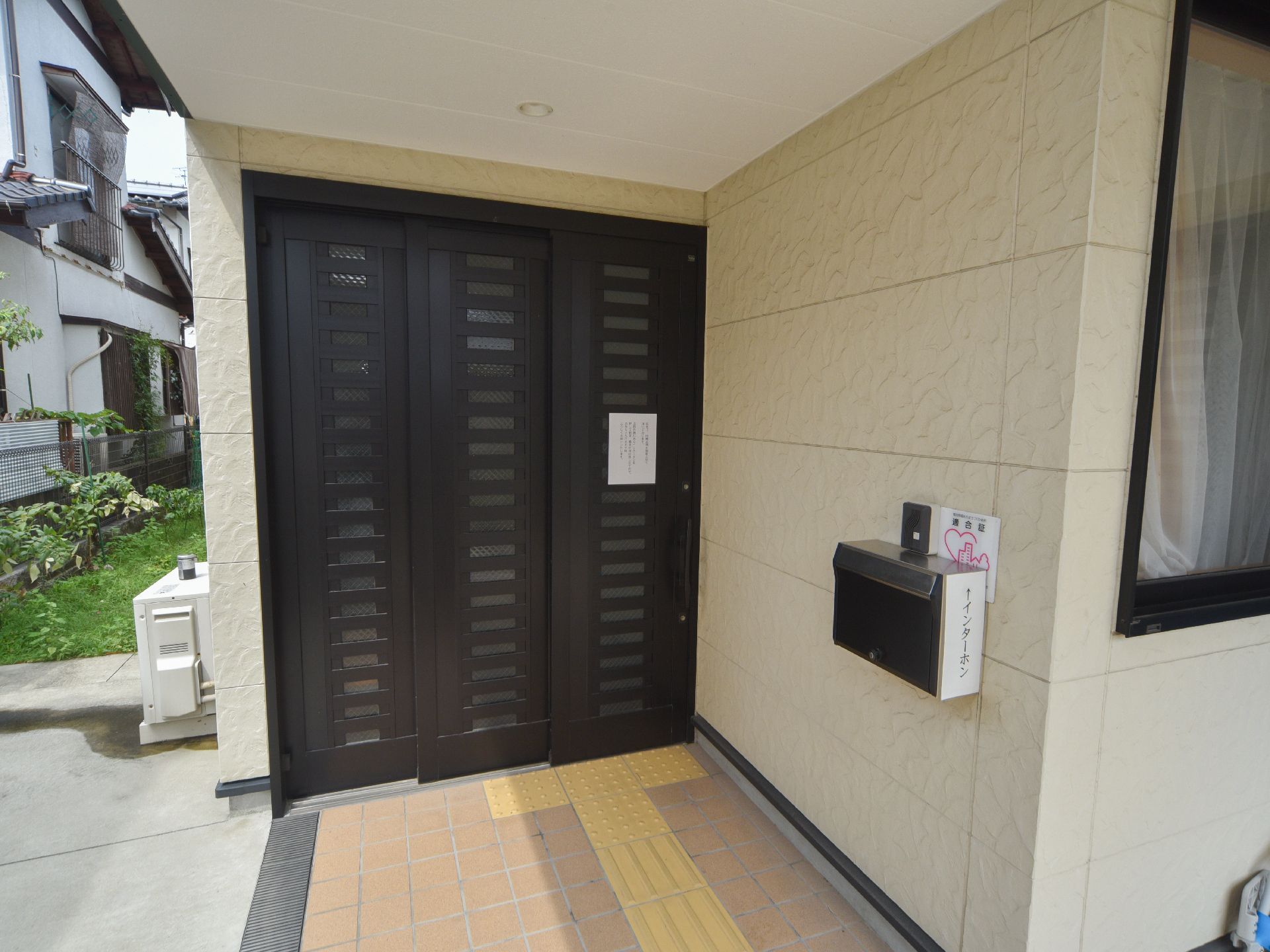 施設の玄関には、横開きのドアが付いている。床には、点字ブロックがある。壁にインターフォンと郵便受けが付いている。