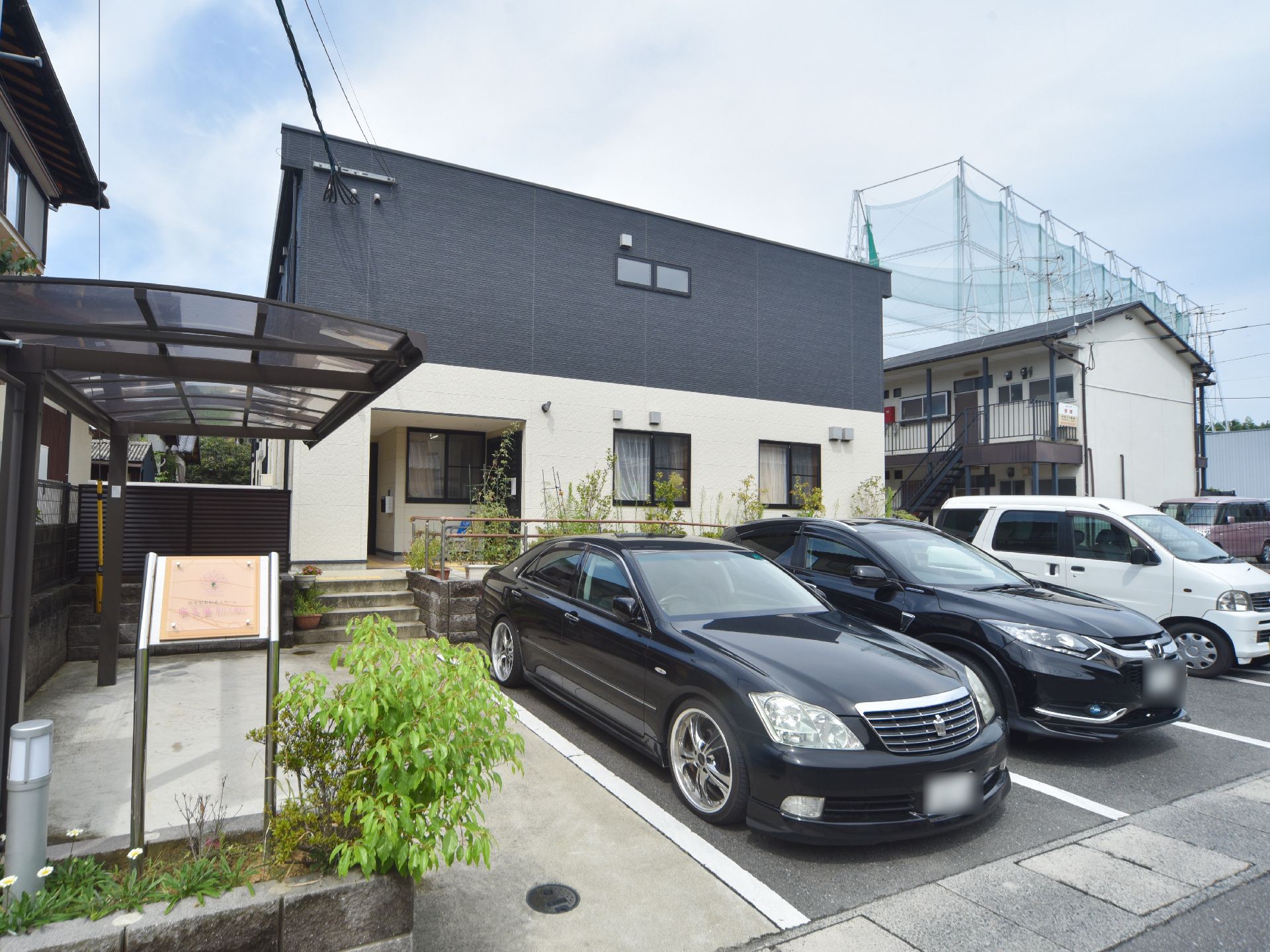 施設の建物前には、駐車スペースがある。向かって左手に屋根付きのスペースがあり、建物につながる階段がある。