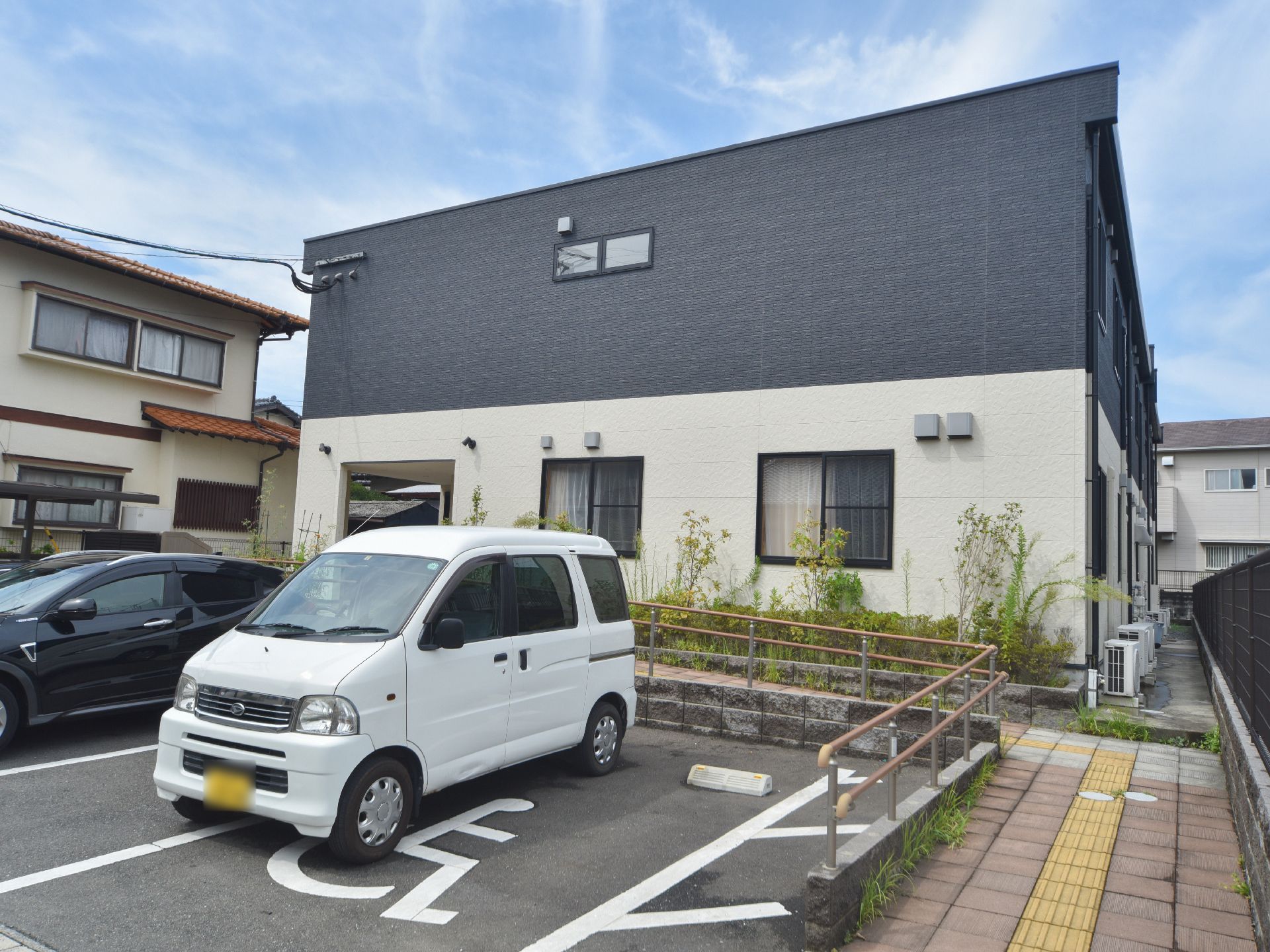 建物の右手にはスロープ状の歩道があり、玄関につながっている。スロープには、手すりと点字ブロックが設置されている。