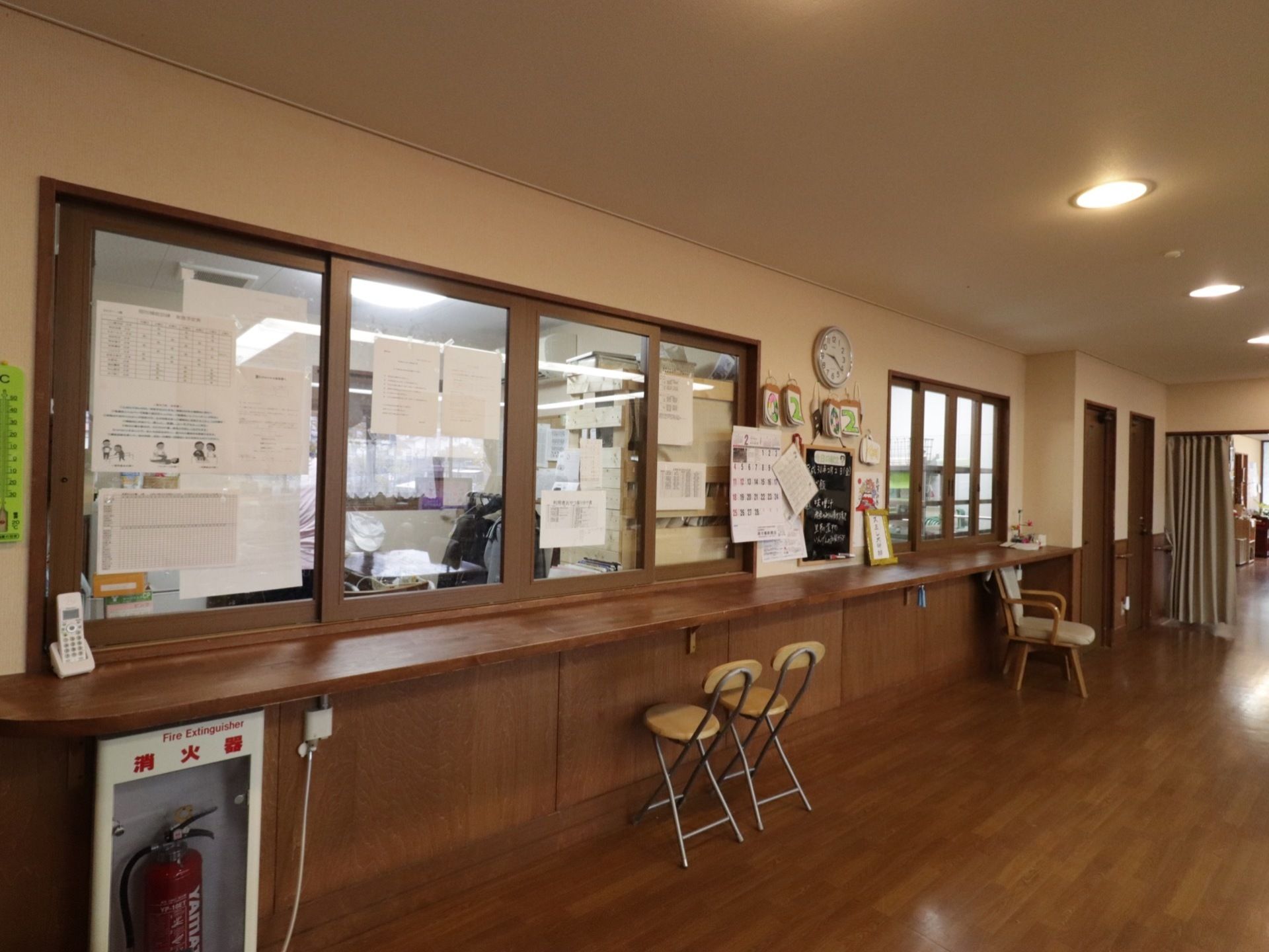 大きな窓で仕切ってある。受付の前にはカウンターが付いている。消火器が設置してある。椅子が何脚か置いてある。