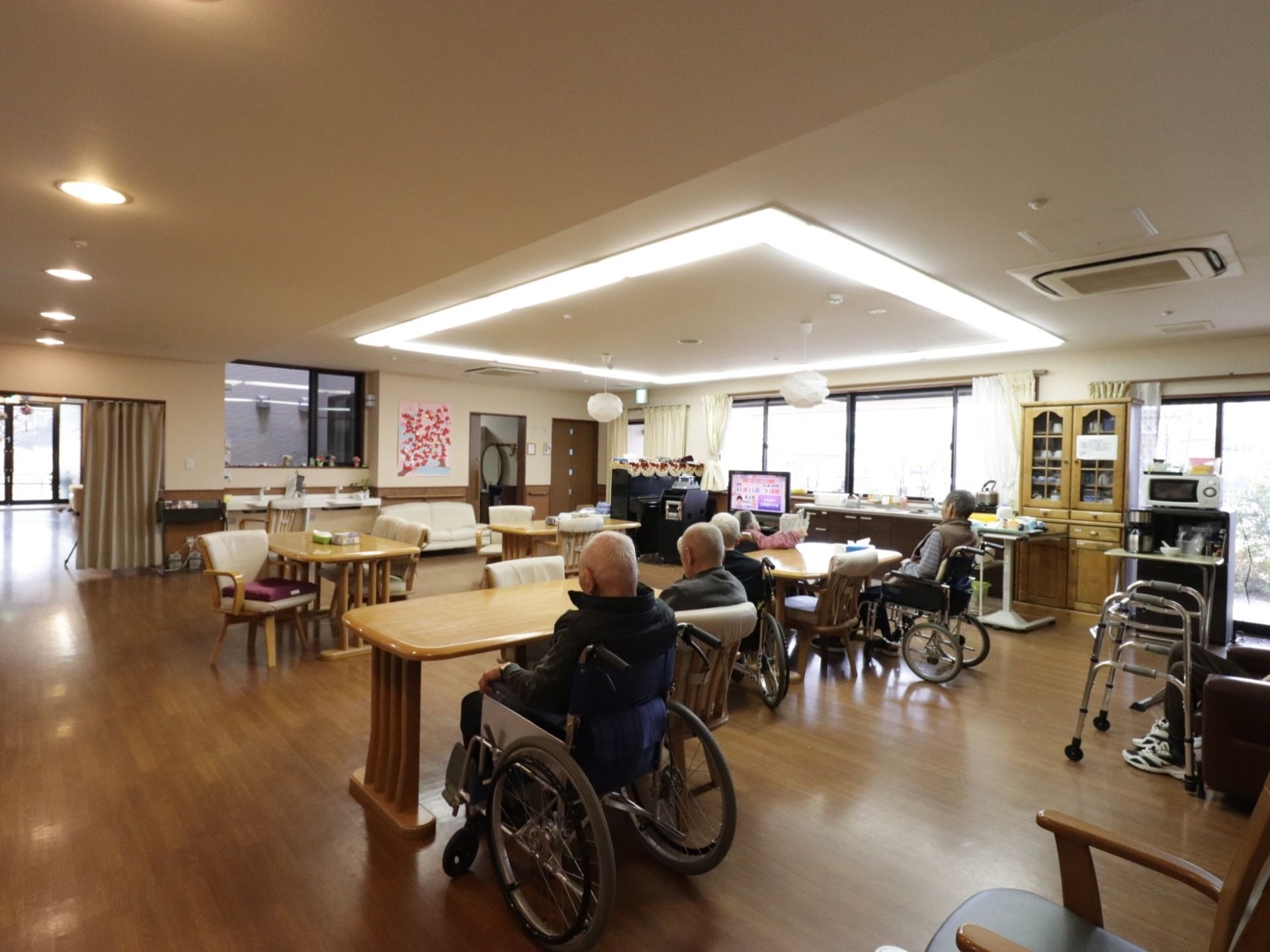 大きなスペースでダイニングセットが4セット置いてある。三人掛けソファが奥に方に置いてある。ピアノが置いてある。