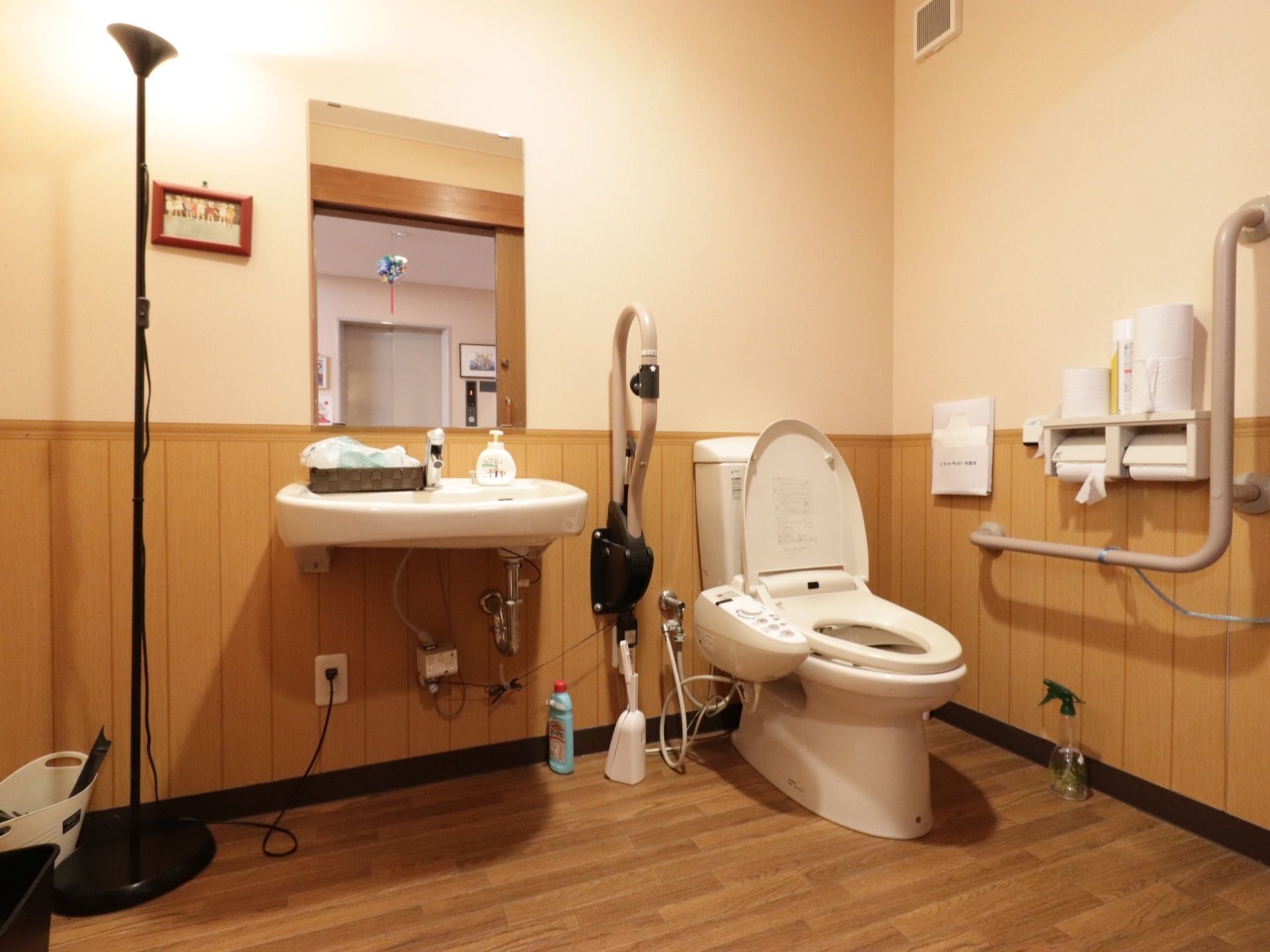 共同トイレ。便器には温水便座が設置されている。L字型手すり、跳ね上げ式の手すりがあり、車椅子でも移乗しやすいように配慮している。