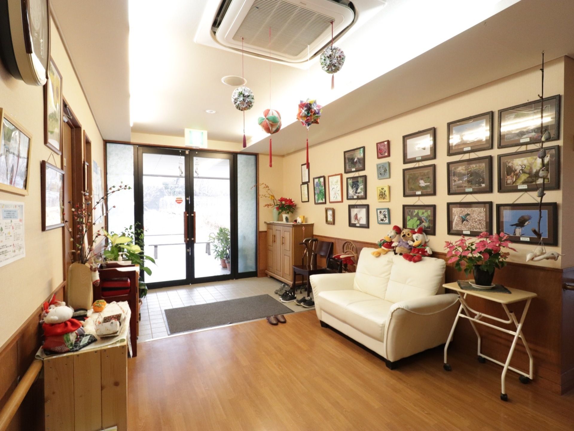 玄関の扉はガラス製で、十分な採光がある。野鳥の写真や入居者様の作品が展示され、アットホームな雰囲気である。