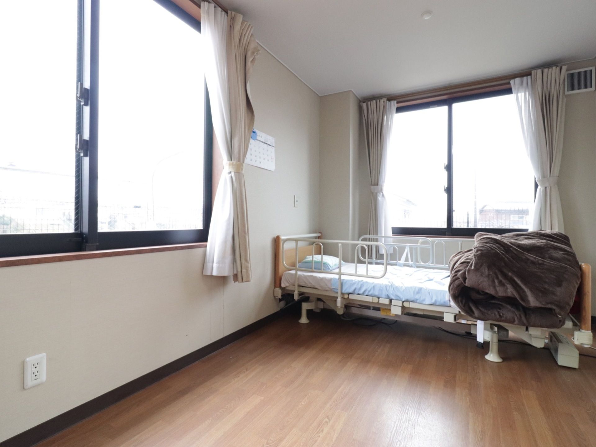 居室には２か所の窓があり、日当たりが良い。介護用ベッドが置かれているが、快適に生活できる十分な広さがある。