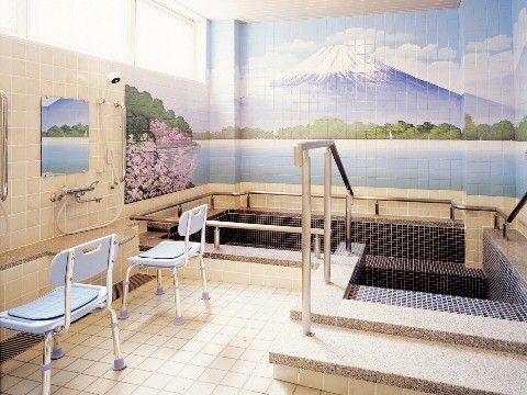 富士山と桜の描かれた壁と、手すりや段のついた浴槽のある浴室