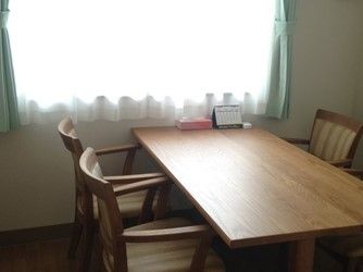 窓際に４人掛けのダイニングテーブルセットが置かれている。卓上には小さなカレンダーとティッシュが用意されている。