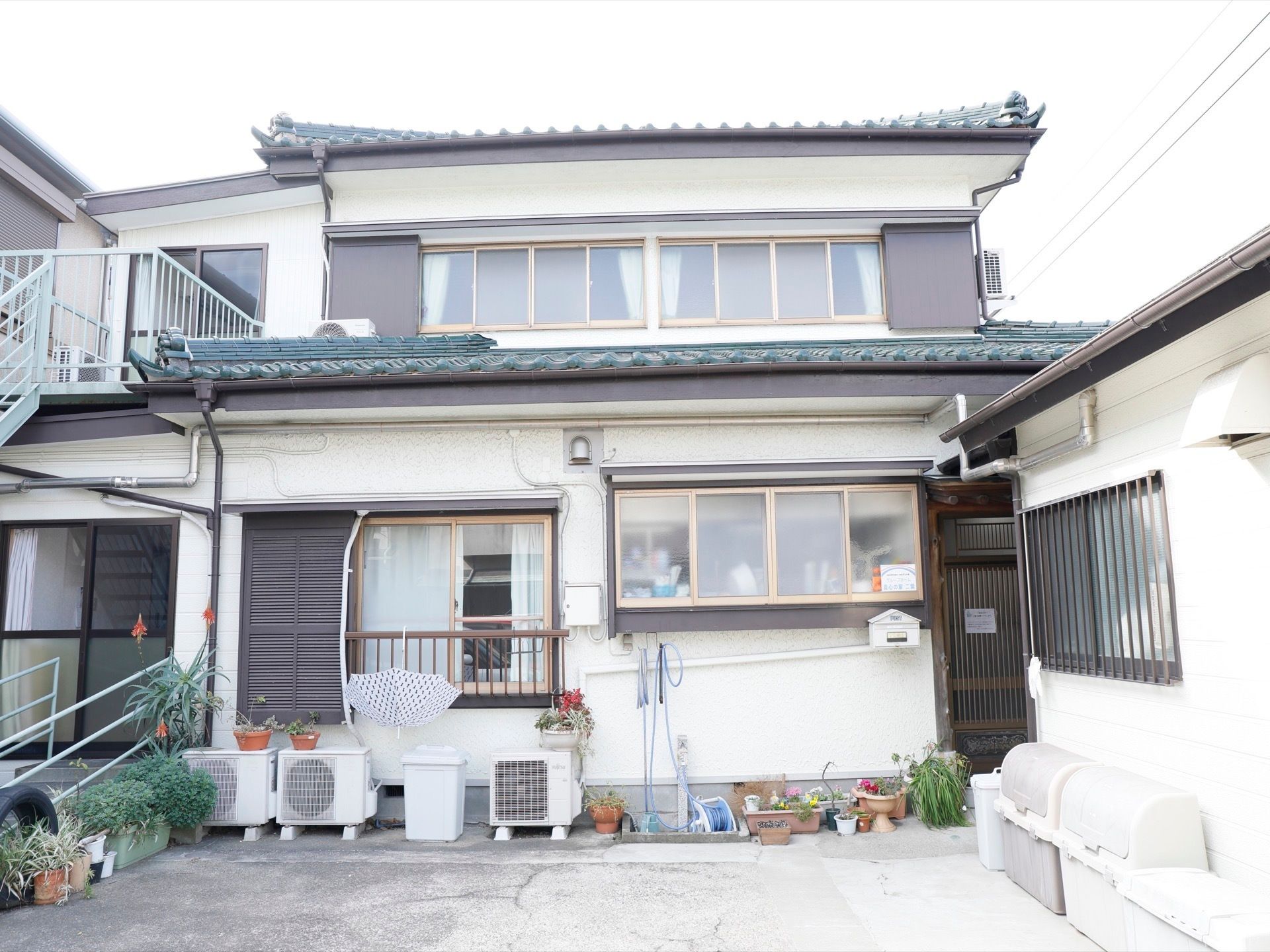 一般の民家のような外観をした施設。安全に出入りができるように階段に手すりが設置されている。２台分の駐車スペースがある。