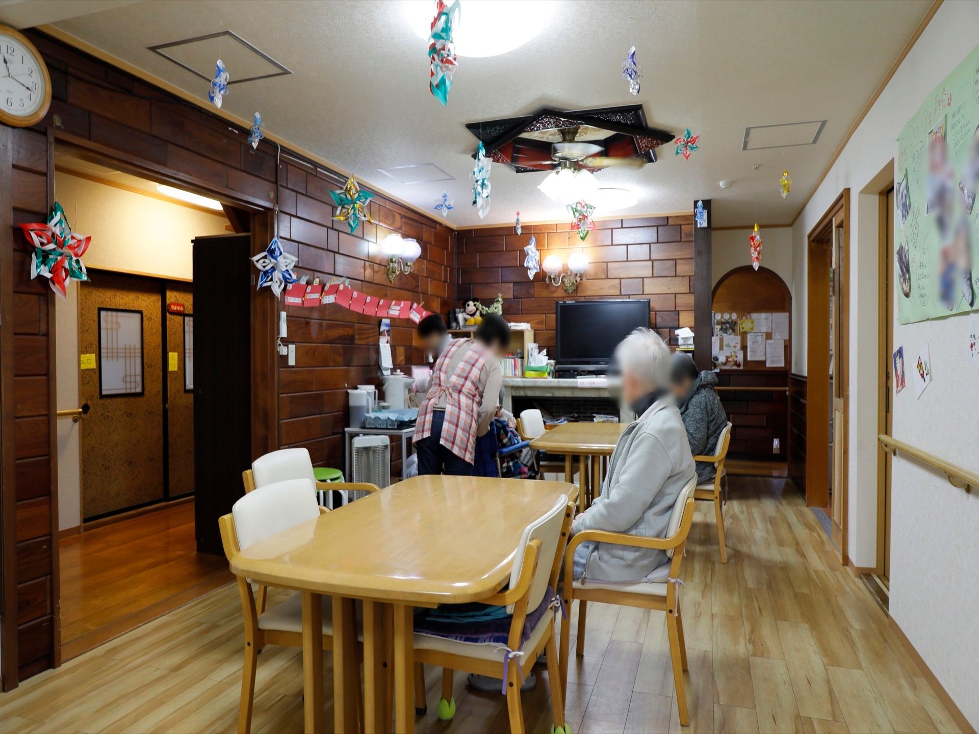 食堂に、ひじ掛け付きの椅子とテーブルが配置されている。大型テレビやポットが用意されている。壁には折り紙作品などが展示されている。