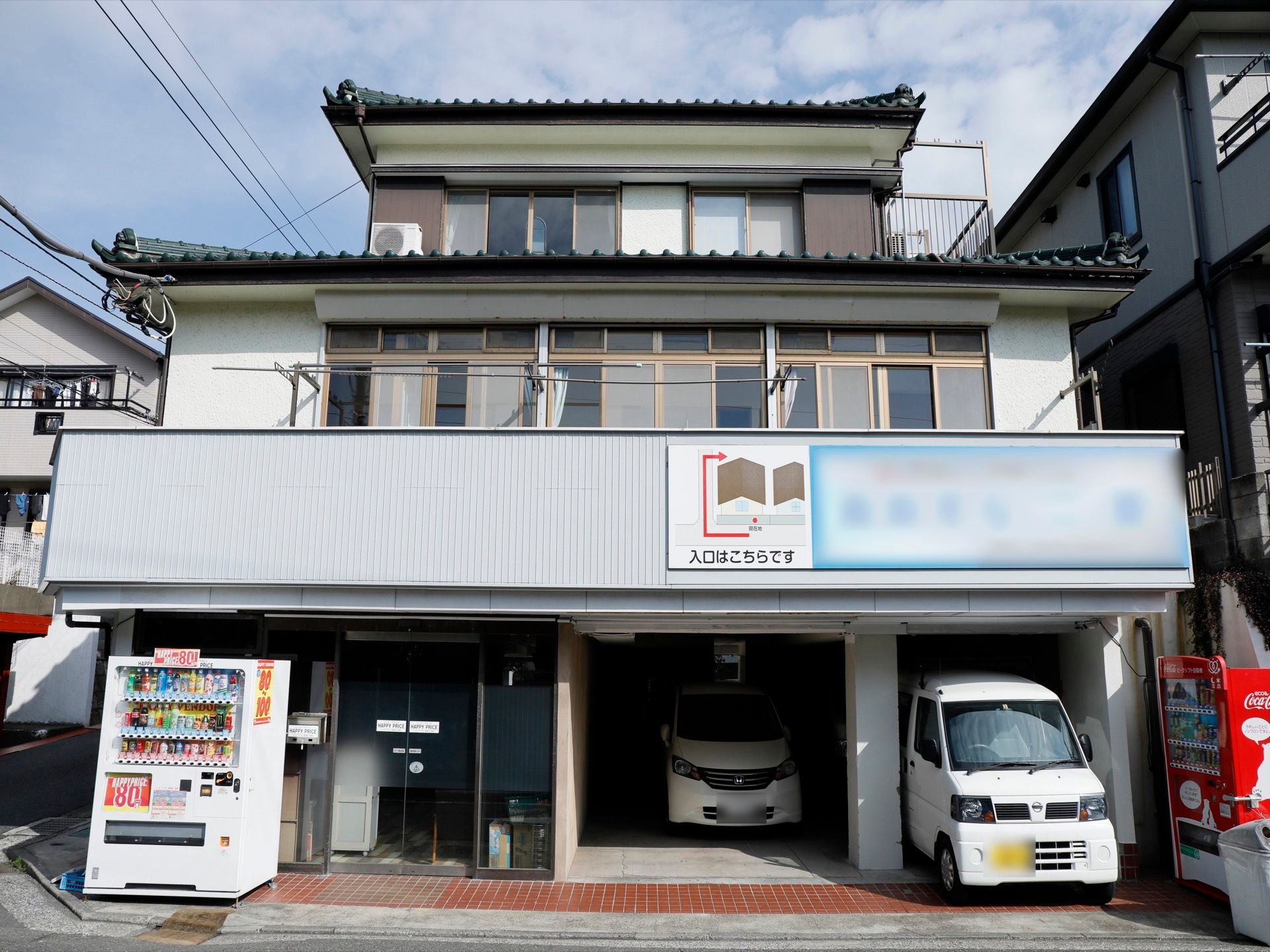 日当たりのいい２階のベランダに物干しざおが置かれた瓦屋根の3階建ての建物