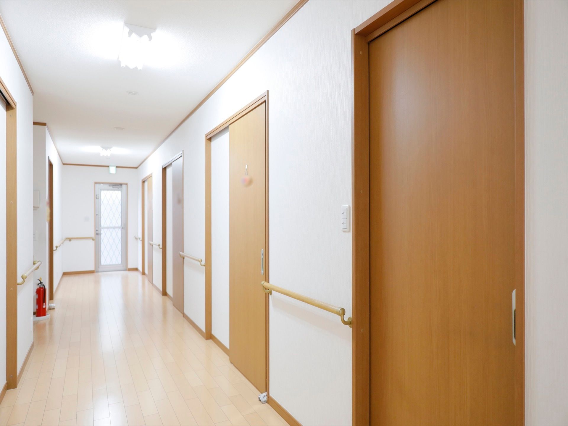 バリアフリーで明るい廊下。居室扉の間に手すりが設置されて、安心して通行することができる。スライドドアで衝突の心配がない。