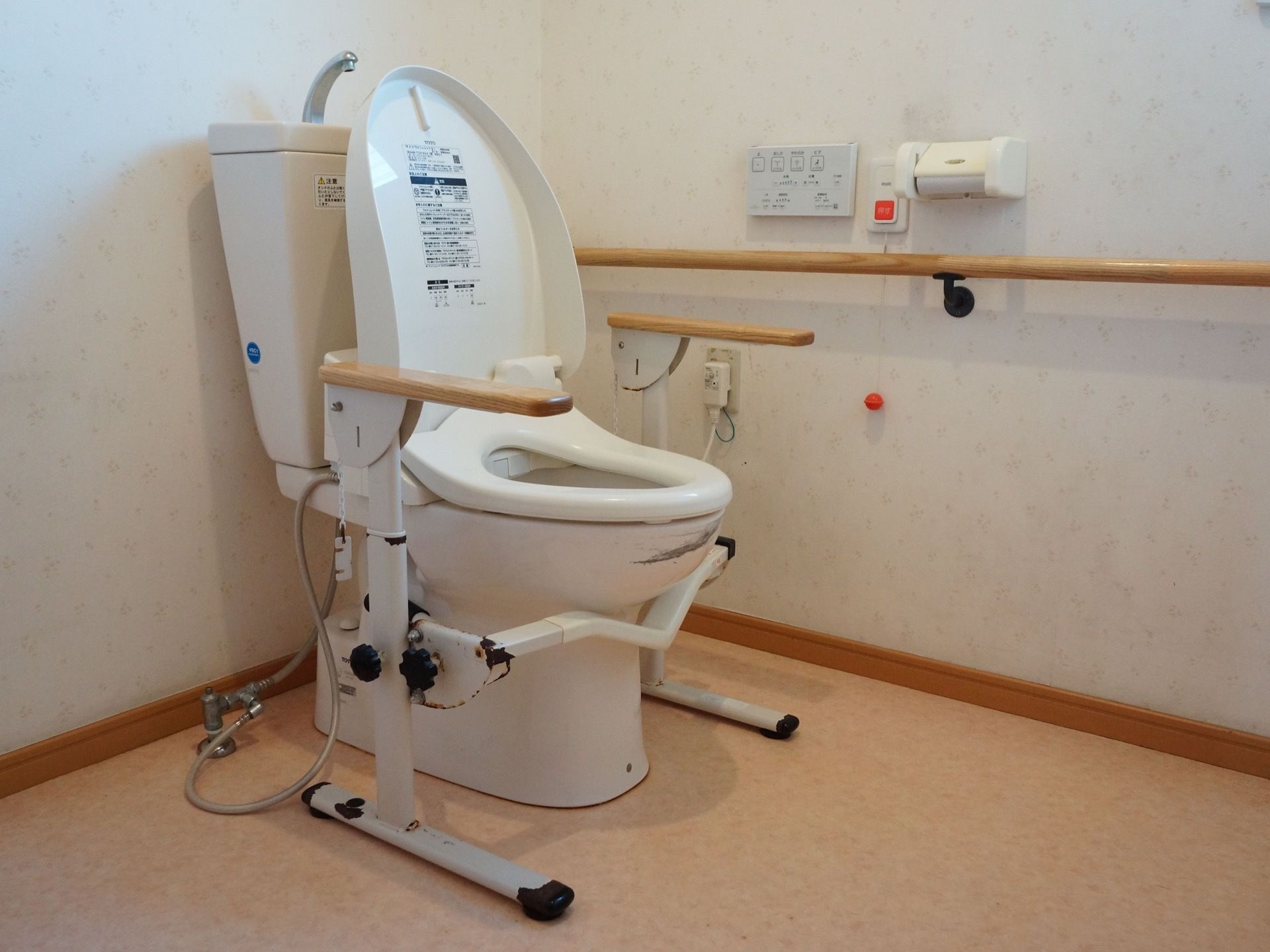 車椅子のまま入れる広いトイレである。手洗いタンク付きの便器には、立ち座りの動作に便利な手すりが設置されている。