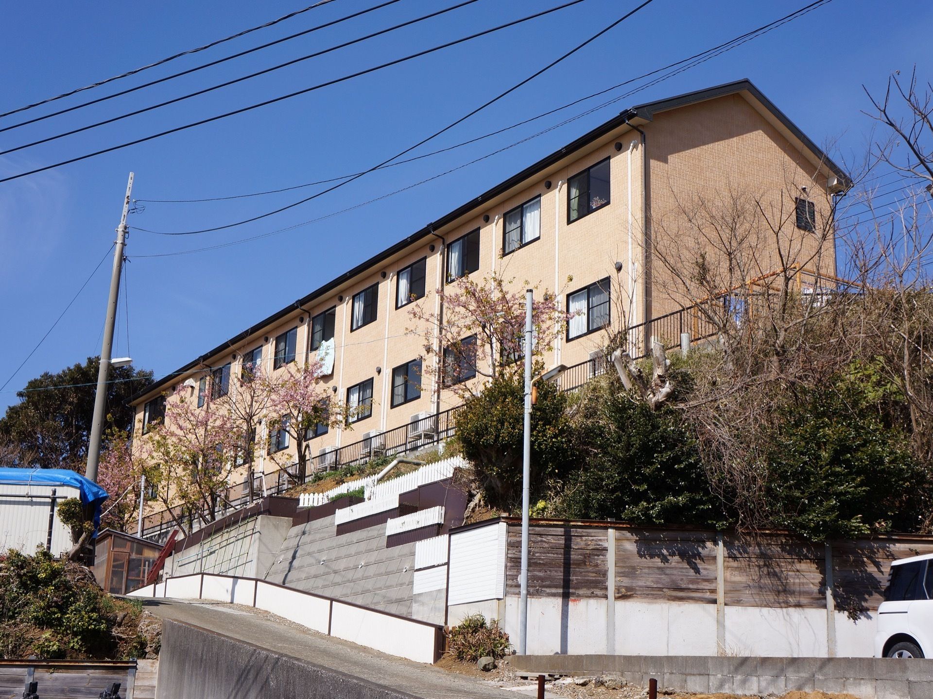自然に囲まれた高台に建っているベージュ色の２階建ての施設である。広い駐車場が道路近くに設けられている。