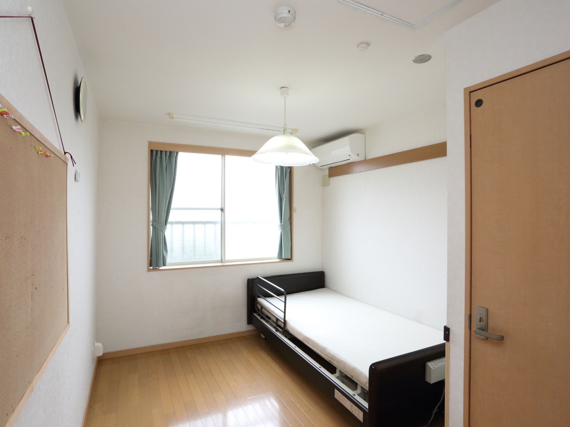 介護用ベッドがある。壁には時計が掛けられている。室内にトイレがある。エアコンが完備されている。腰高窓がある。