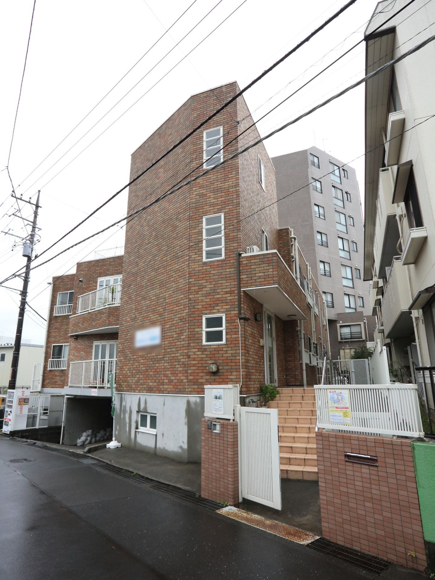 レンガの外壁で、入り口には門扉が設置されている。玄関までは手すりつきの階段がある。施設名の看板が外壁に掛けられている。