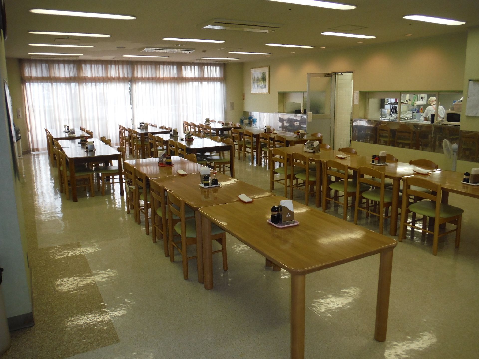 広々とした食堂。四角いテーブルが複数並べて置かれ、それぞれのテーブルの上に調味料などがまとめて置かれている。