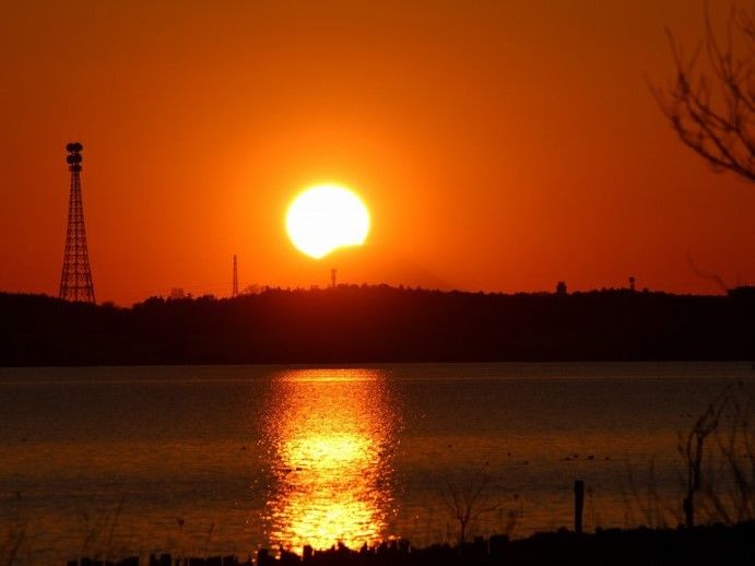 空全体が真っ赤に染まっているほどの強烈な夕焼け。中心には太陽があり、その光が手前にある湖に映り込んでいる。