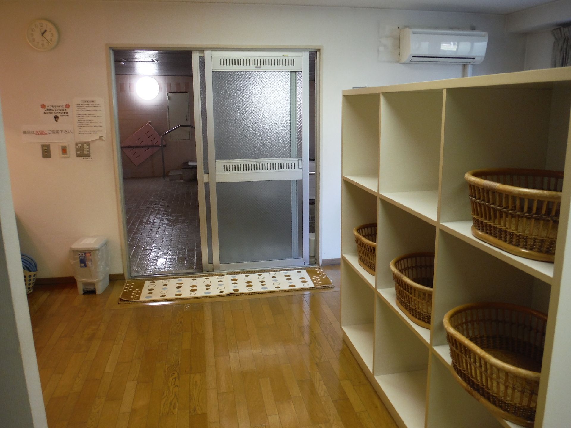右側に棚があり、脱衣カゴが置かれている部屋。すりガラスのドアが開いており、奥にある浴室が見えている。