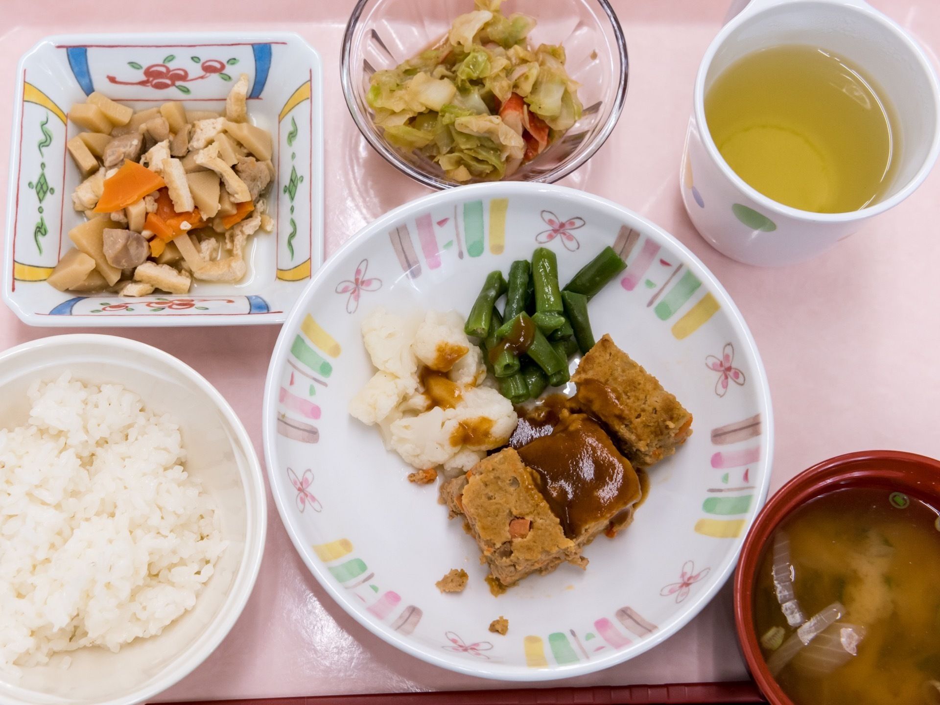 1人分の食事メニューの一例である。主菜1品と副菜2品で、ご飯と味噌汁のほかにお茶を添えている。食材は食べやすく刻んでいる。