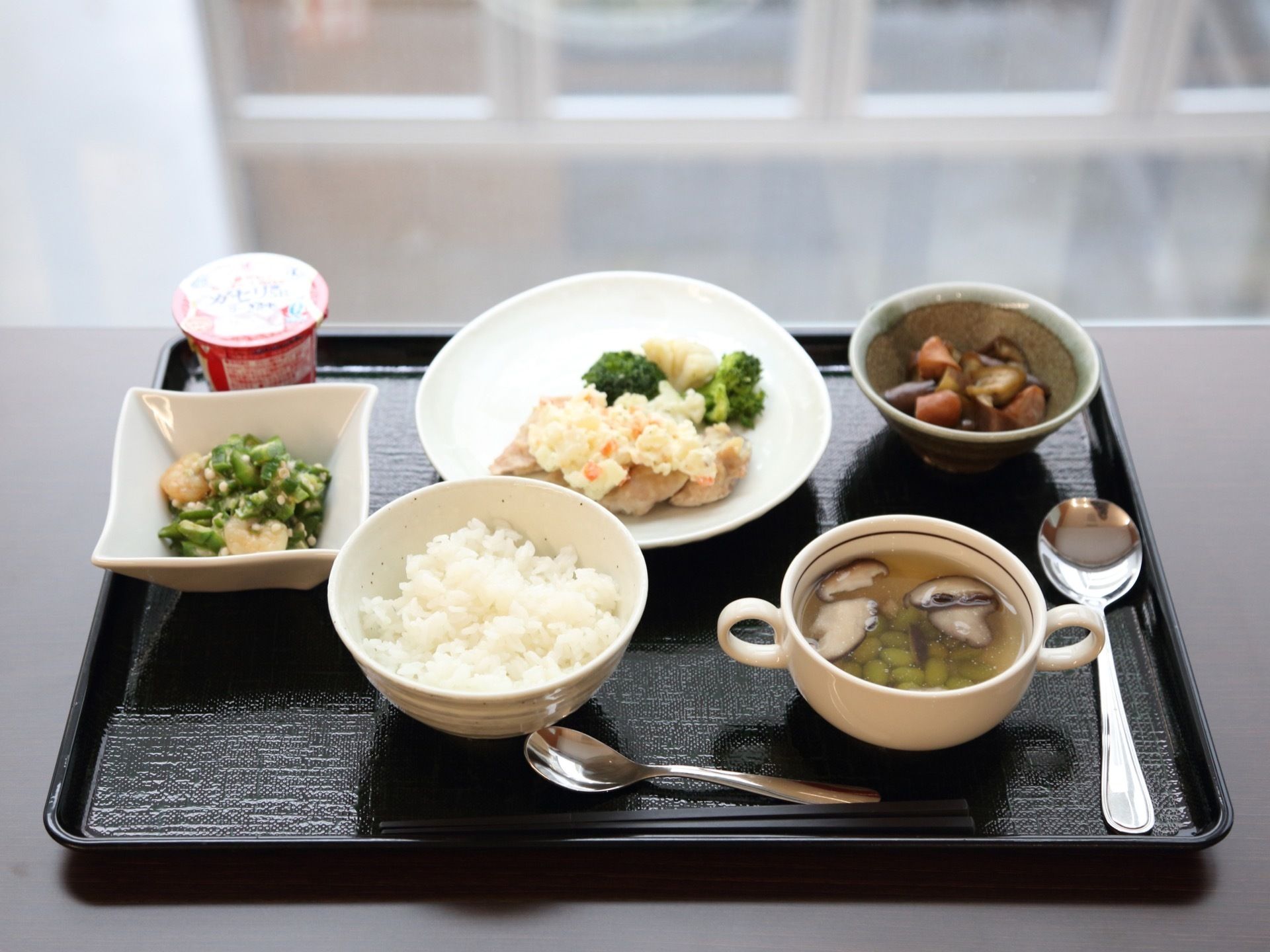 黒のトレーの上に、ご飯と汁物、メインのおかずに２つの小鉢、デザートをセットした食事である。お箸と大きさの異なるスプーンを２つ添えている。