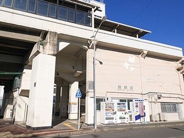 白色を基調とした最寄り駅の外観である。線路、駅のホームは高架になっている。自動販売機が複数台設置されている。
