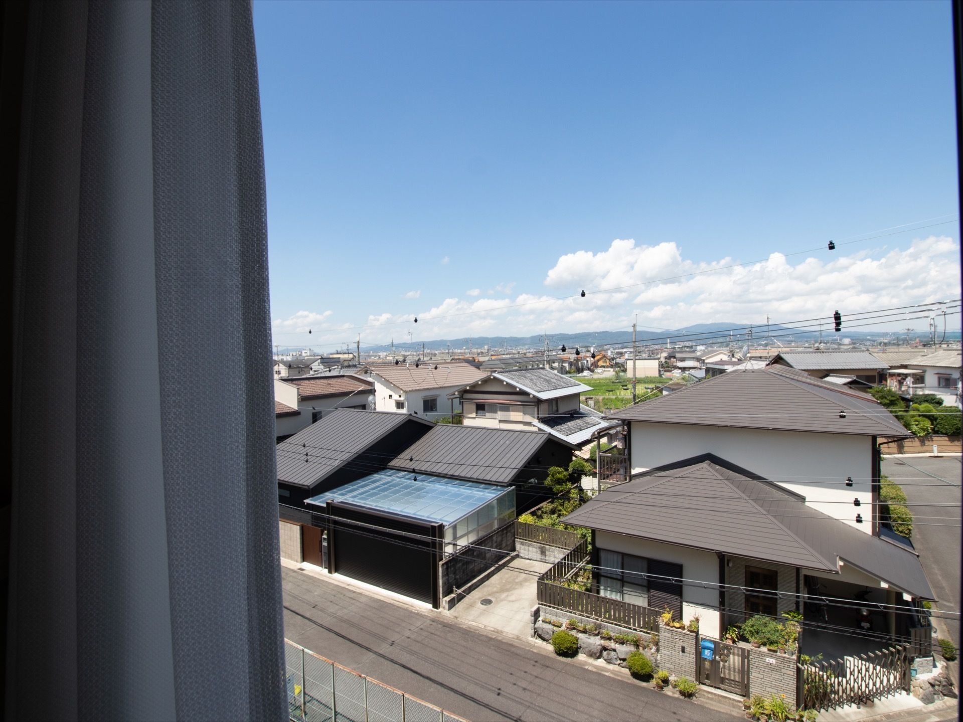 住宅地に施設はあり、遠くには青空とともに山が連なって見えている。住宅地の中にも木が植えられ、緑に溢れている。