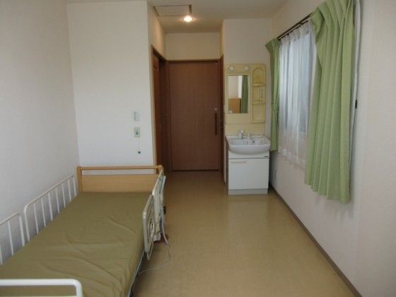 介護用ベッドと洗面台が設置された緑のカーテンの居室