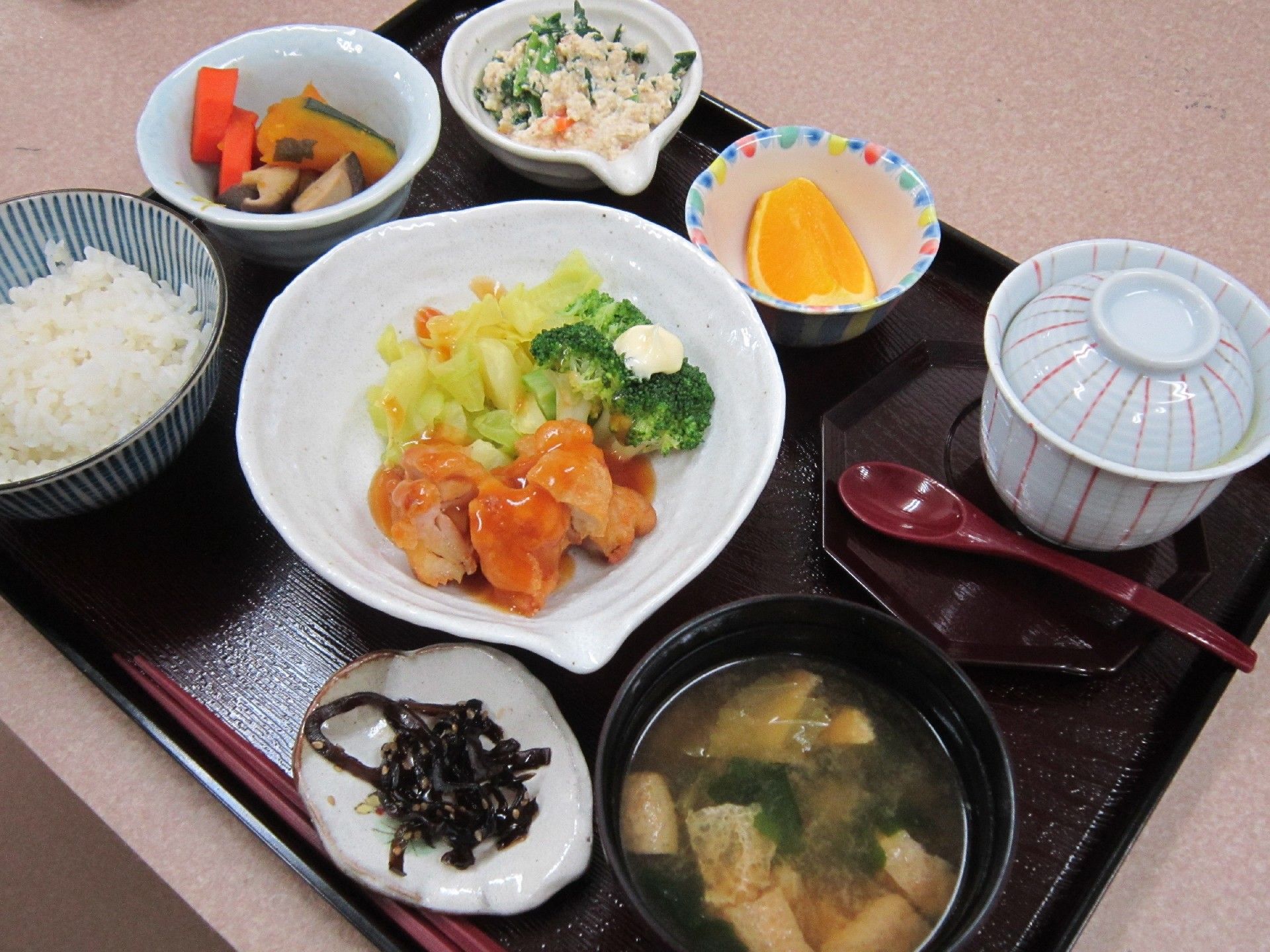 膳の上には、茶碗によそわれたご飯、野菜が添えられた副菜、煮物、漬物、茶碗蒸し、味噌汁、フルーツが置かれている。