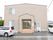 木造２階建てのグレーの建物の玄関正面に自動販売機がある。入口へのアプローチは、階段とスロープがあり手すりがついている。