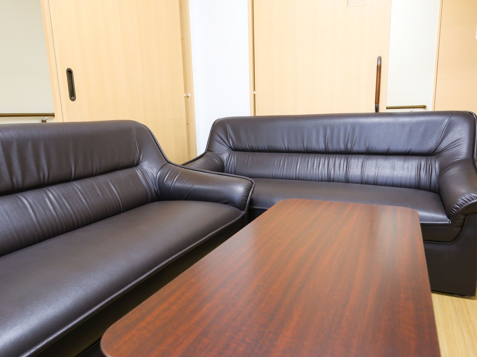 フローリングの部屋に黒い革張りのソファが２つ置かれている。ダークブラウンのテーブルがあり、落ち着いた空間になっている。
