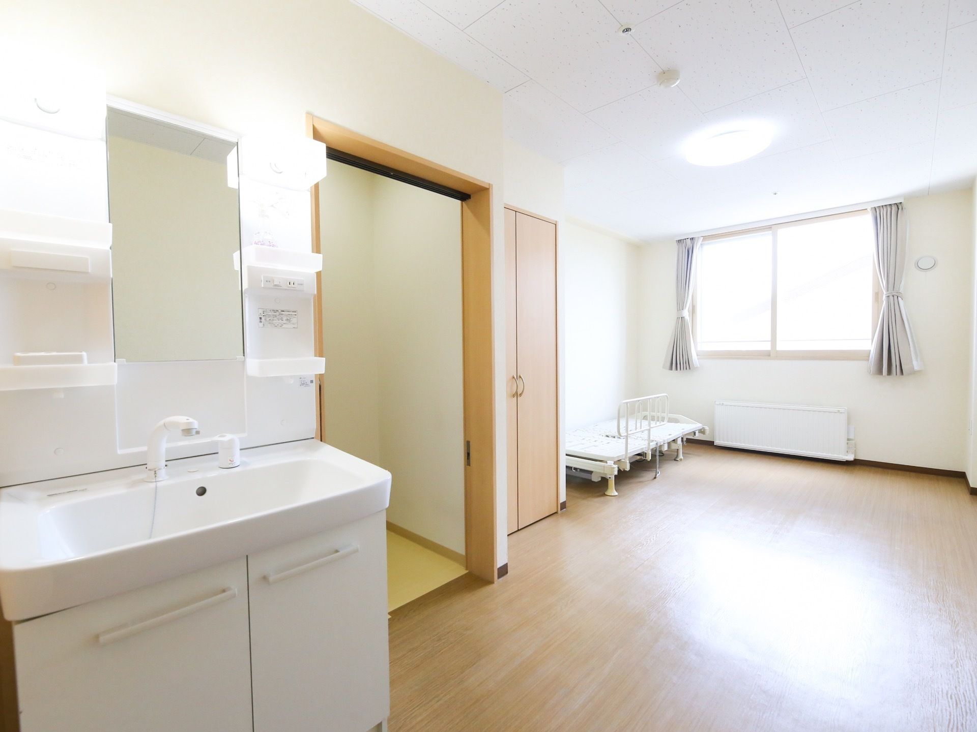 フローリングの部屋に、洗面台が設置されている。部屋の奥にはクローゼットがあり、その横に電動ベッドが置かれている。
