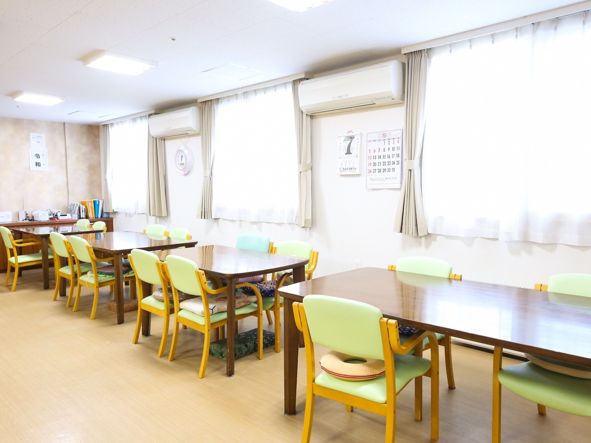 窓から陽射しが入って明るい食堂がある。ダイニングテーブルが並べられていて、椅子にはクッションが乗せられている。