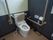 フローリングの床の上に白い洋式トイレが設置されている。壁には青い細かい目のタイルがたくさん貼られている。