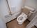 背もたれが付いた洋式便器があり、壁に非常ボタンと２連のトイレットペーパーホルダーと手すりが設置されている。