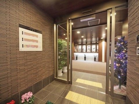 焦げ茶色の壁と床、ひさしに囲まれた玄関は、扉がガラスの自動ドアになっている。建物内までは平坦に繋がっている。