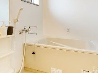 清潔感あふれる白色の浴室である。洗い場には鏡、シャンプーやボディソープが置ける棚が備え付けられている。