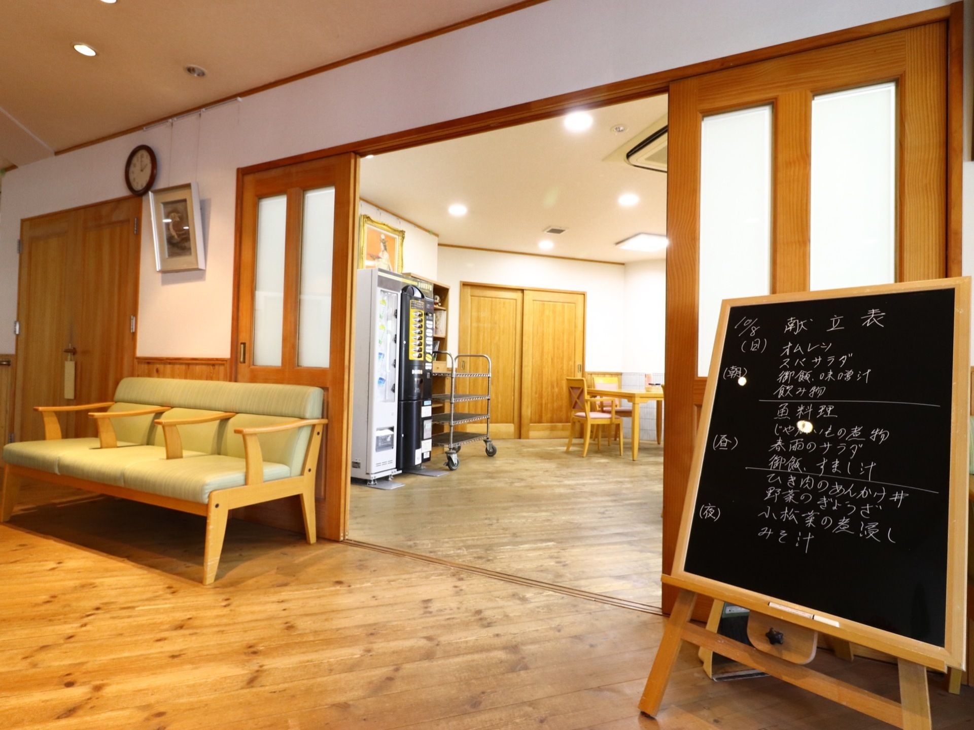 大きな引き戸の食堂の前の壁際に、べンチが置かれている。また黒板が立っていて、その日1日の献立が書かれている。