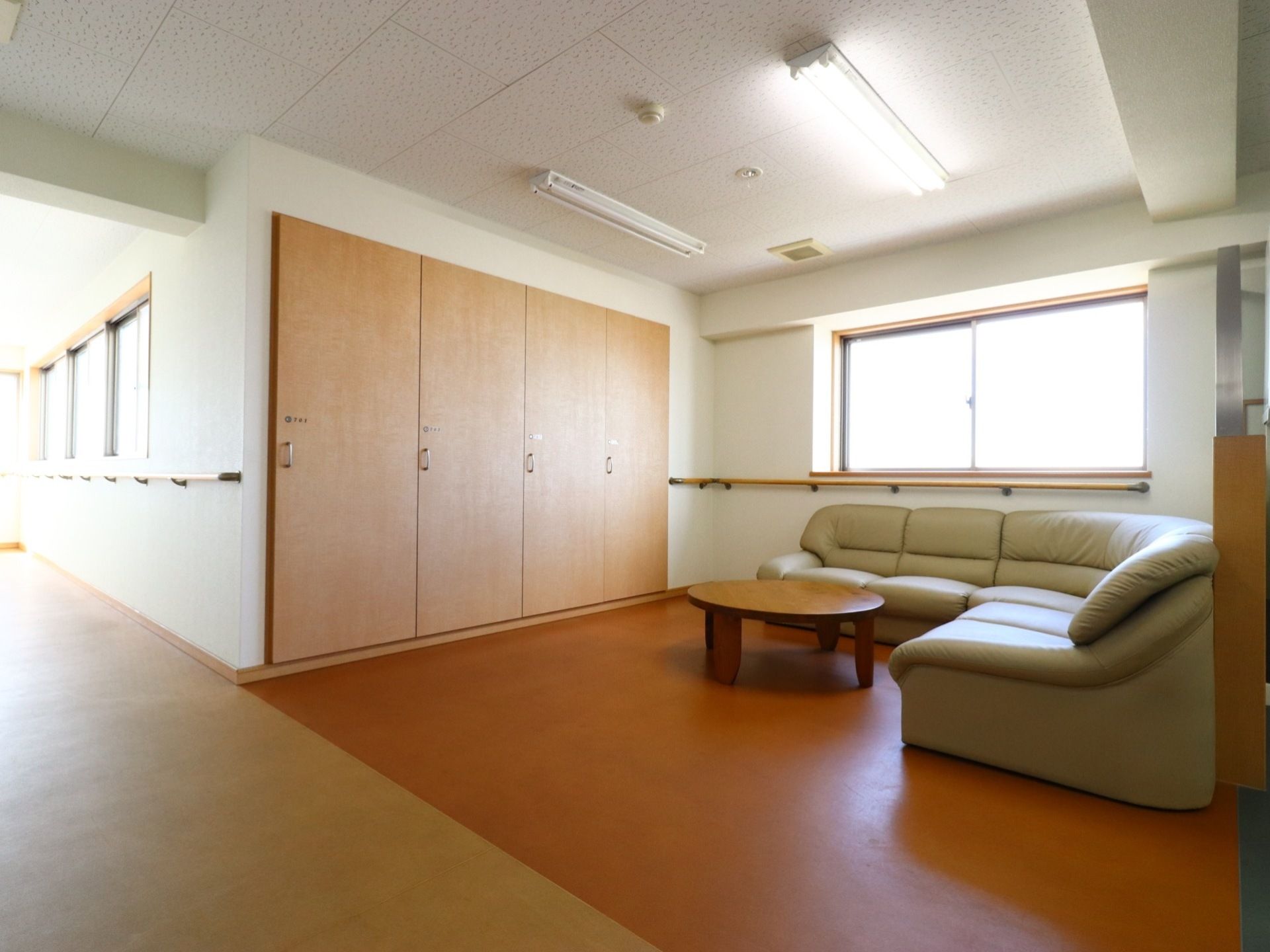 L字型のゆったりしたソファーと、丸テーブルが置かれている。窓があり明るいスペースである。壁に手すりが設置されている。