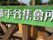 看板は、鮮やかな緑色の板に白い立体文字で書かれており、茶色の木に取り付けてあるのでよく目立っている。周辺には樹木や民家の屋根が見えている。