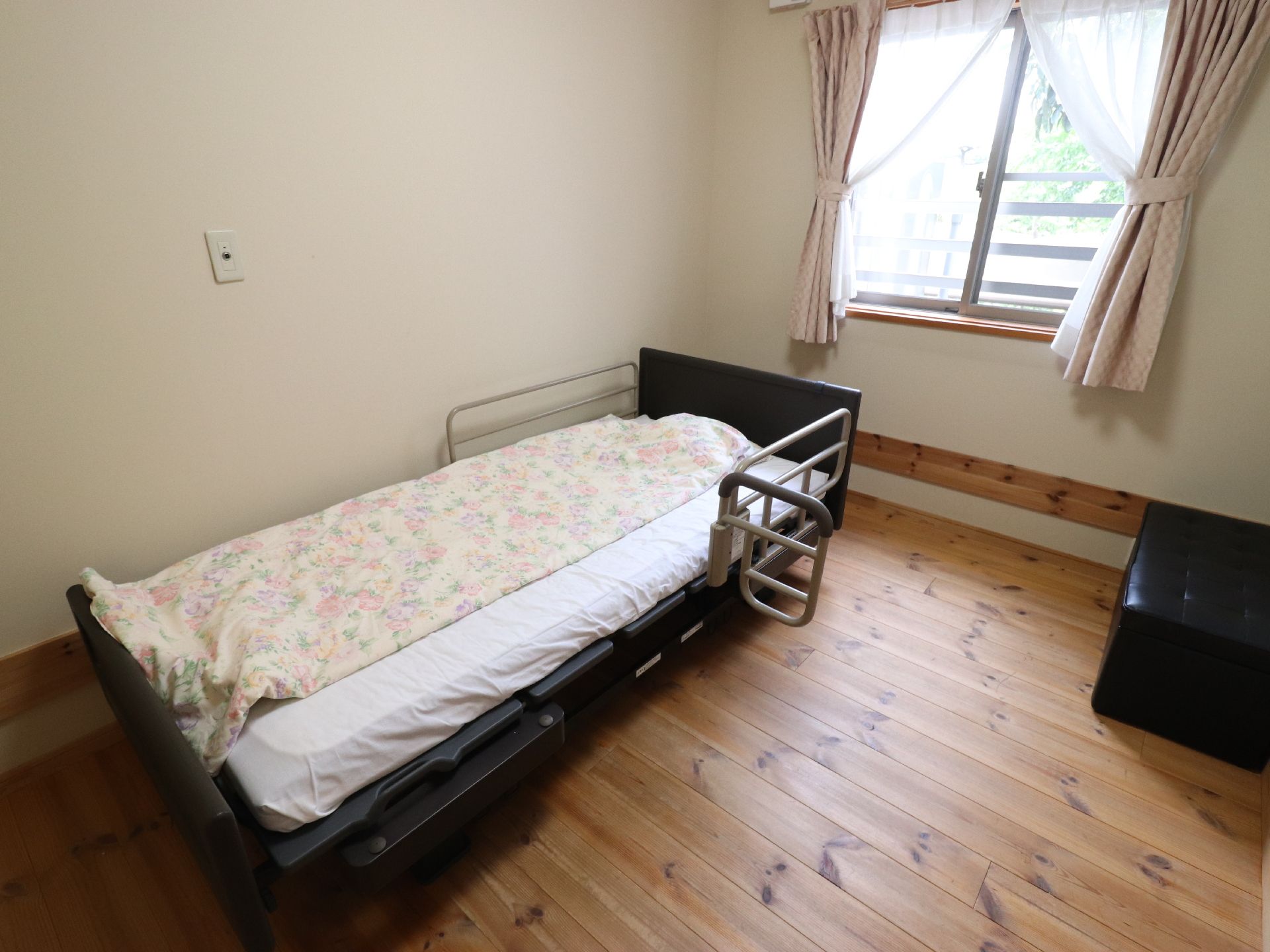 居室の床は、木製の板が敷かれている。壁は、白色である。部屋の中に、ベッドと黒いソファー椅子が置かれている。