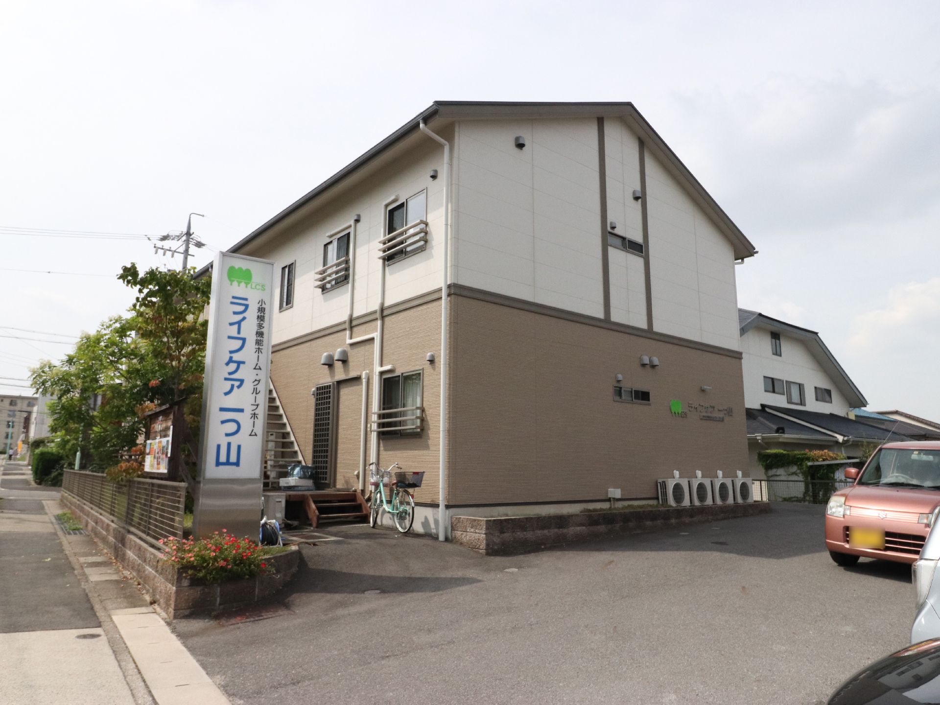 大きな看板が敷地の入り口に設置されたベージュと白の２階建て建物
