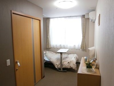 エアコンが完備された日当たりの良い居室である。ベッド近くにキャスター付きのサイドテーブルが置かれている。