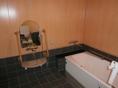 デザイン性のあるお洒落な浴室である。木のぬくもりを感じられる壁で、床は黒を基調としたタイル張りとなっている。