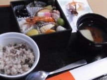 黒塗りの箱膳の中にはさまざまな種類のおせち料理が少しずつ詰められている。お茶碗には赤飯が盛られている。