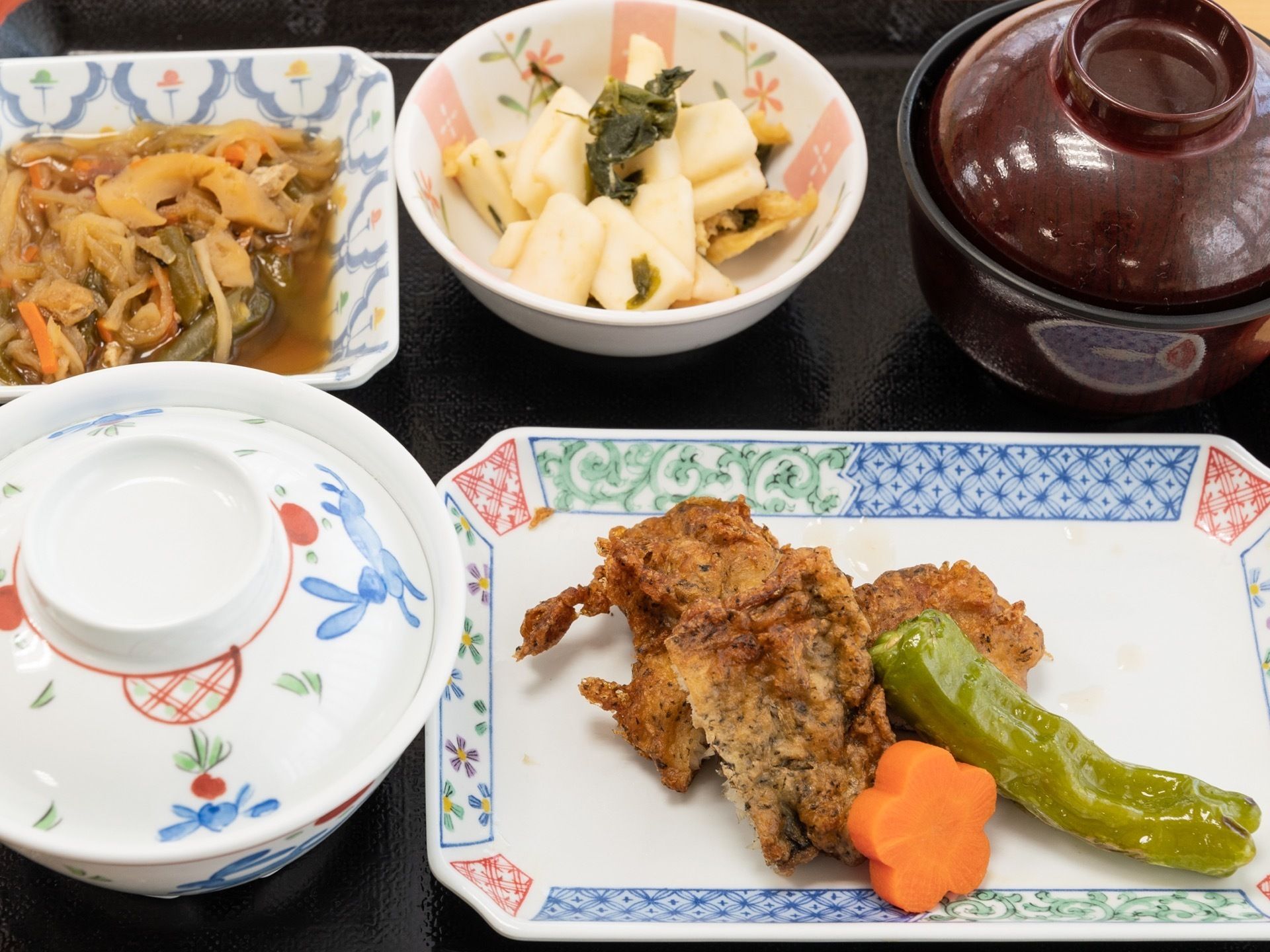 黒い漆塗り風のトレーに、野菜をふんだんに使った料理の小皿が載せられている。茶碗と汁物用の椀には、蓋がされている。