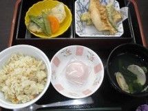 黒いトレーの上に置かれた１食分の食事である。炊き込みご飯と汁物の他に、２品のおかずとゼリー状の料理が並べられている。