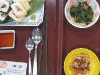 トレーに食事がのっている。メニューは2種類の巻き寿司が笹の葉を敷いた皿に盛り付けられている。副菜として青菜の小鉢や煮豆が配膳されている。