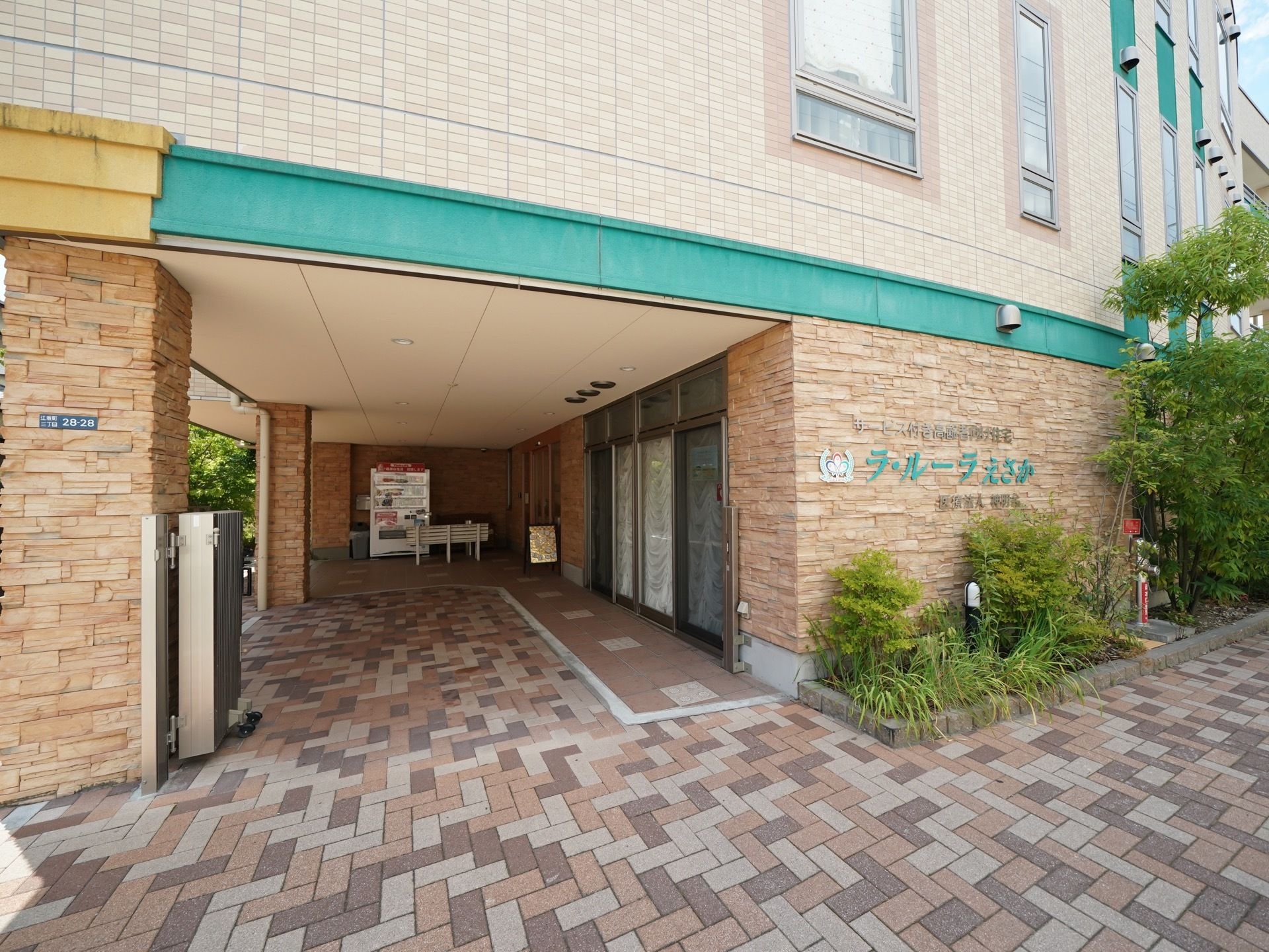 ホテルのような、ゆったりとした入口となっている。入口横の壁には施設名がグリーンの文字で大きく表示されている。