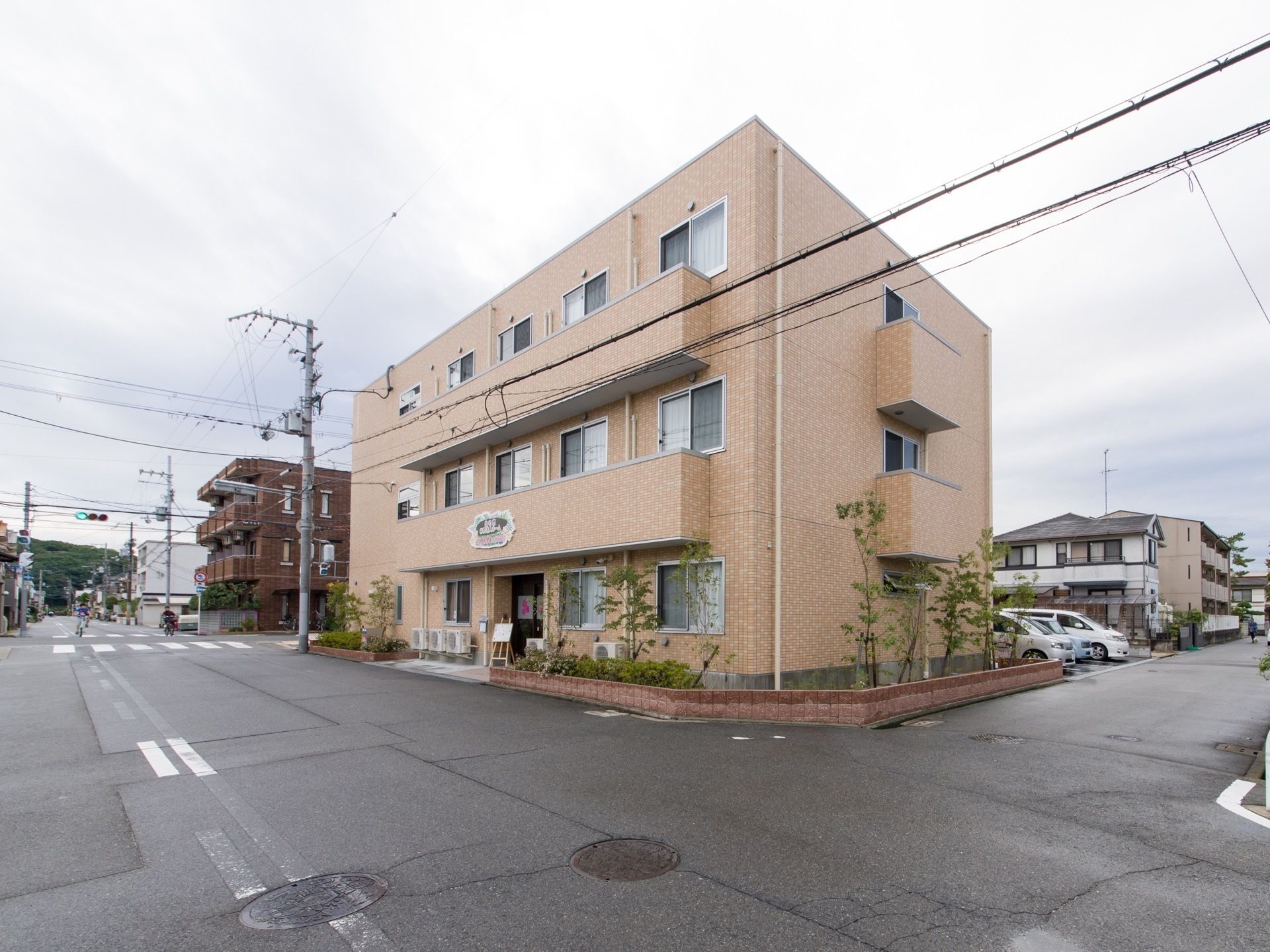 施設の周囲は、沢山の住宅が建つ地区となっている。街並みになじむレンガ調の外壁の3階建ての建物である。周りには花壇があり、木が植えてある。